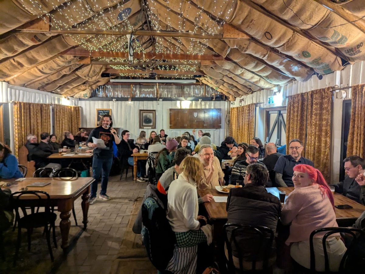 a room full of people sitting at tables listening to a person calling out trivia in a microphone