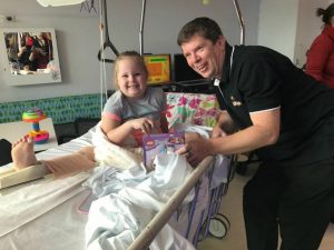 David Boddy, chair of Brick Expo, presents a Lego Friends set to a little girl whose leg is in a splint at Canberra Hospital