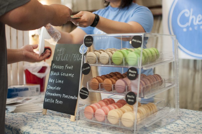Woman in blue t-shirt (face not shown) taking money from man who is buying macarons at a market stall