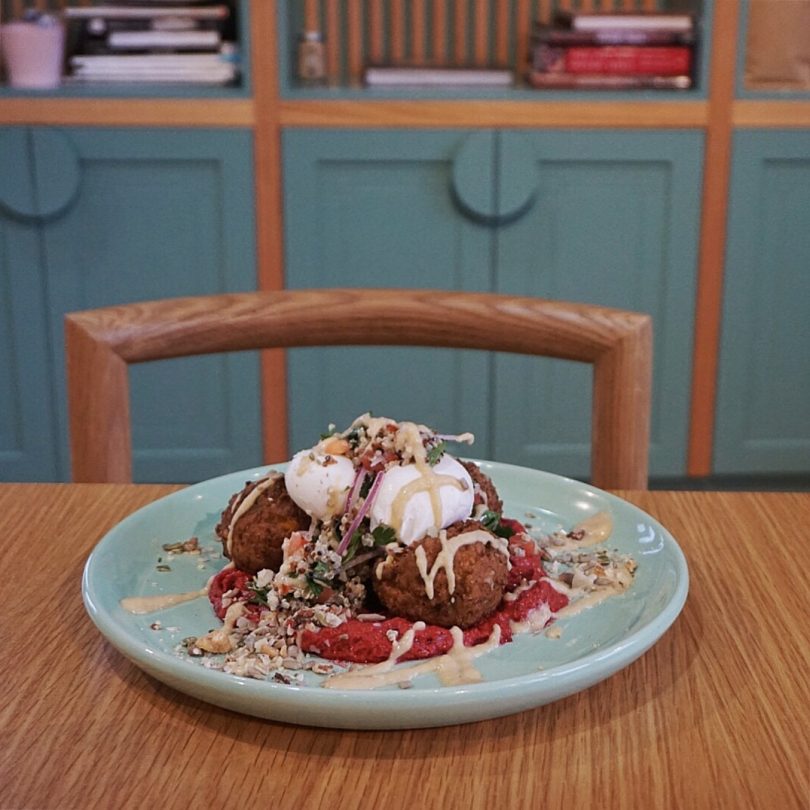 Zucchini, Corn & Haloumi Fritters with poached eggs, quinoa tabbouleh, seeds, beetroot romesco & lemon hummus dressing. Photo: Sophia Brady