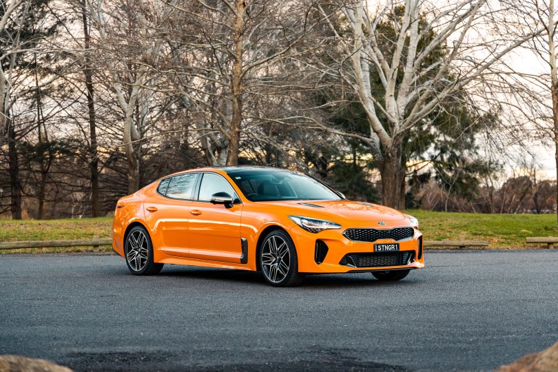 Orange Kia Stinger GT car parked in front of trees