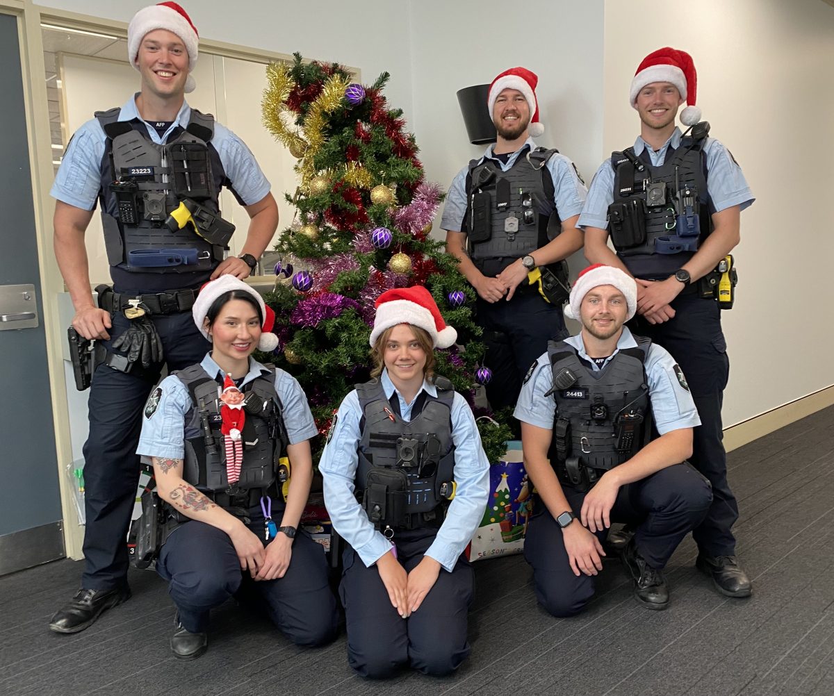 Six police officers in Santa hats around a Christmas tree.