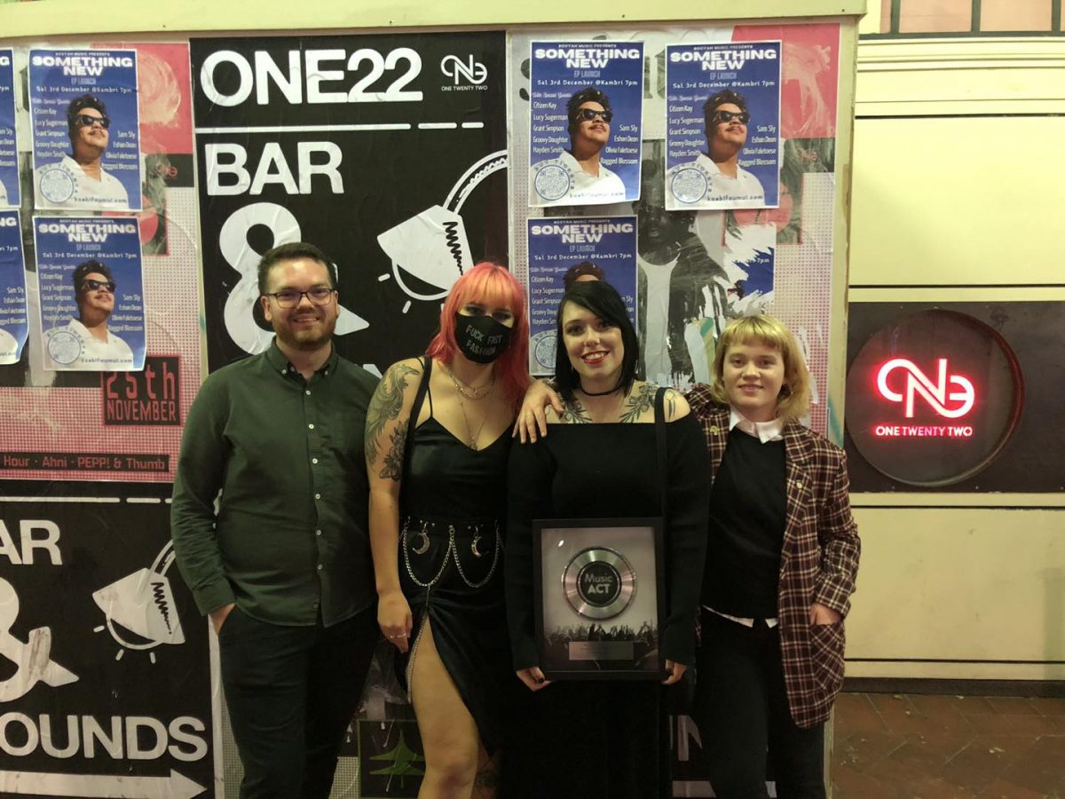 Sarah O'Malley holding her in front of a wall of posters near the bar ONE22 in Civic Canberra.