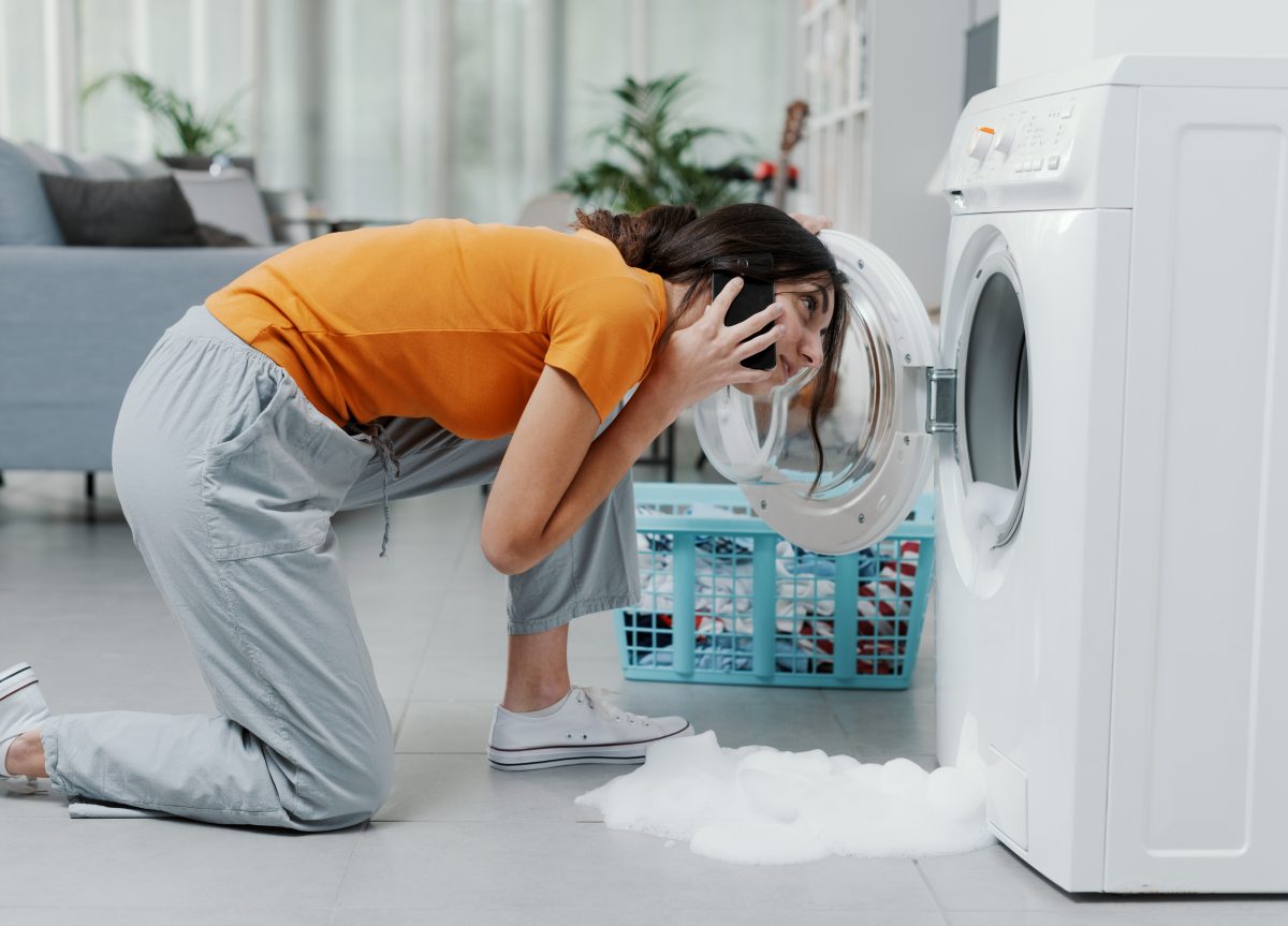 Woman on her mobile phone bends to look into her faulty washing machine