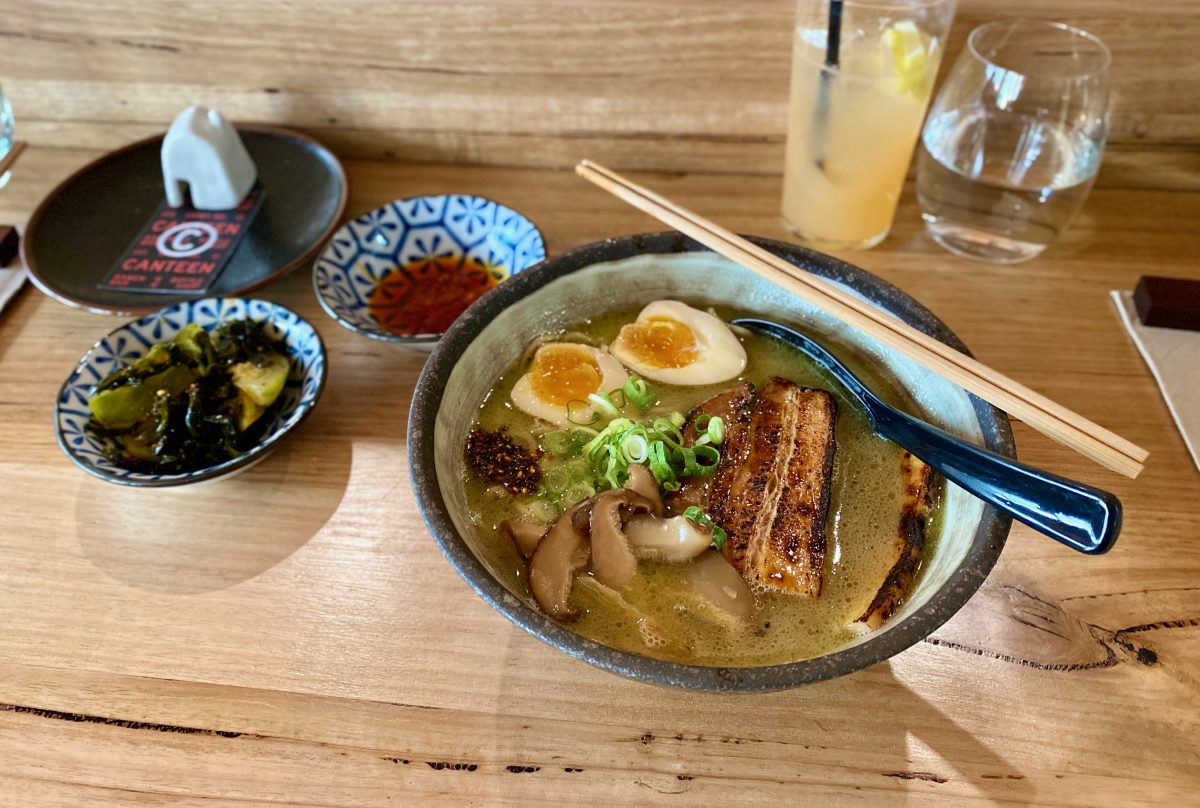 Bowl of Ramen with condiments on wooden bench at Canteen