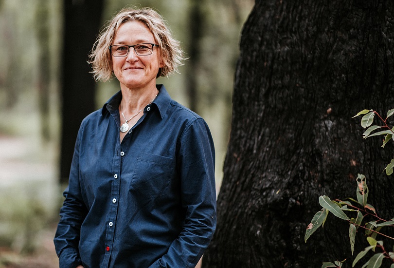 A woman standing outside, a tree to her right