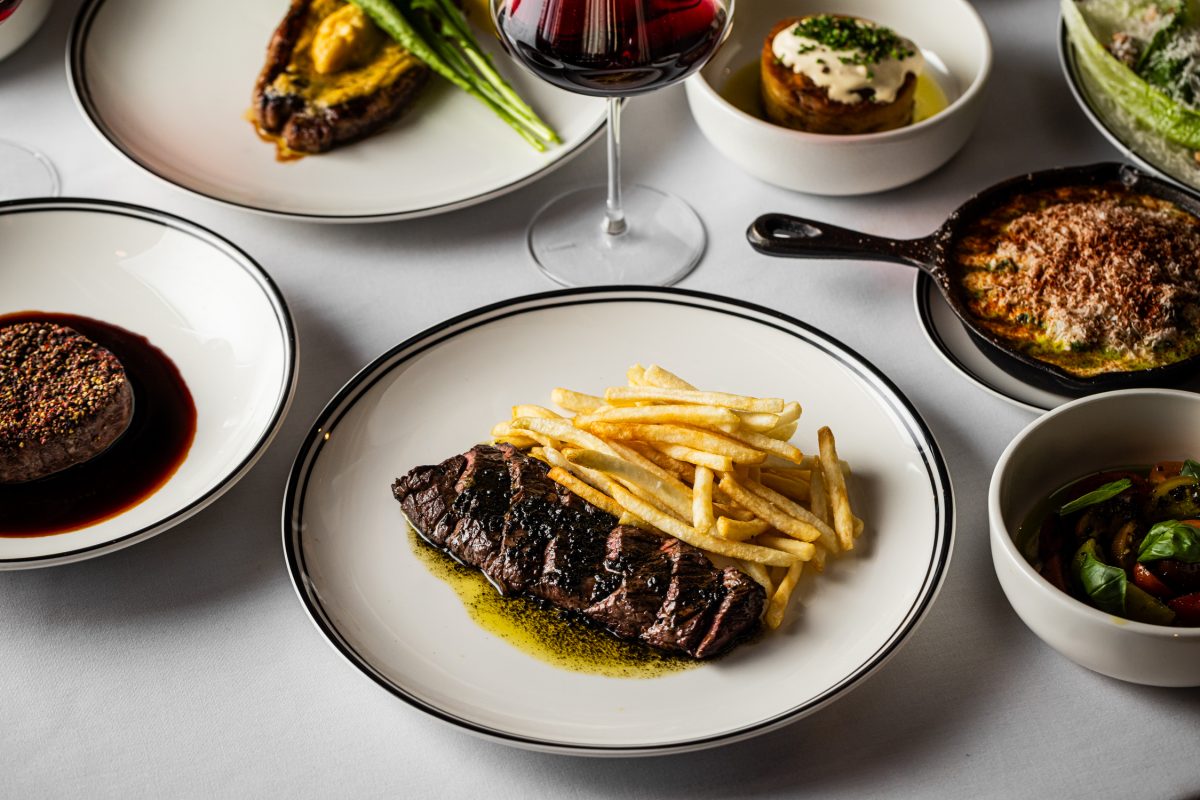 Steak sliced on a plate with fries, other dishes behind