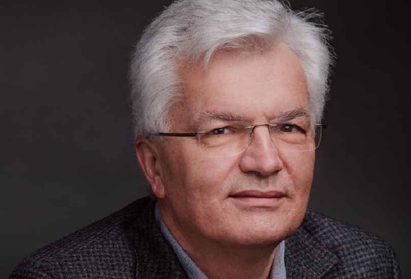 A man with white hair, glasses and a checkered shirt staring at the camera.