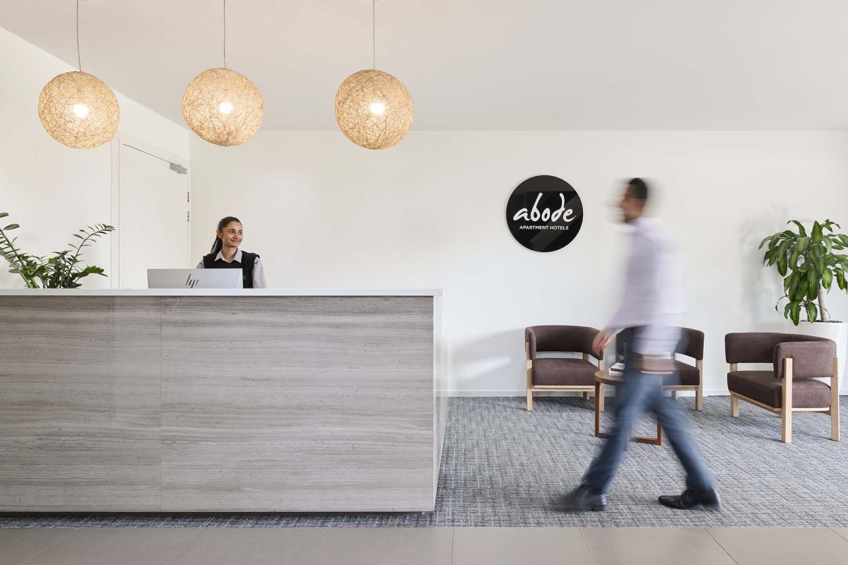 a person walking into an Abode Hotel past a receptionist at the front desk