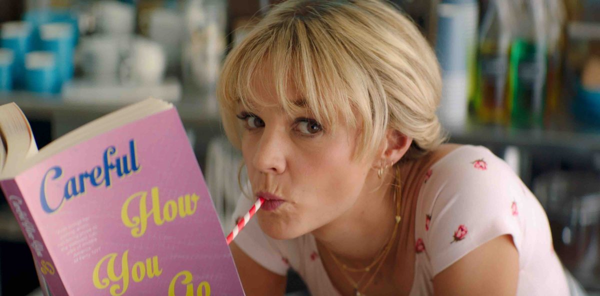 Still from Promising Young Woman showing a woman reading a book and drinking from a straw