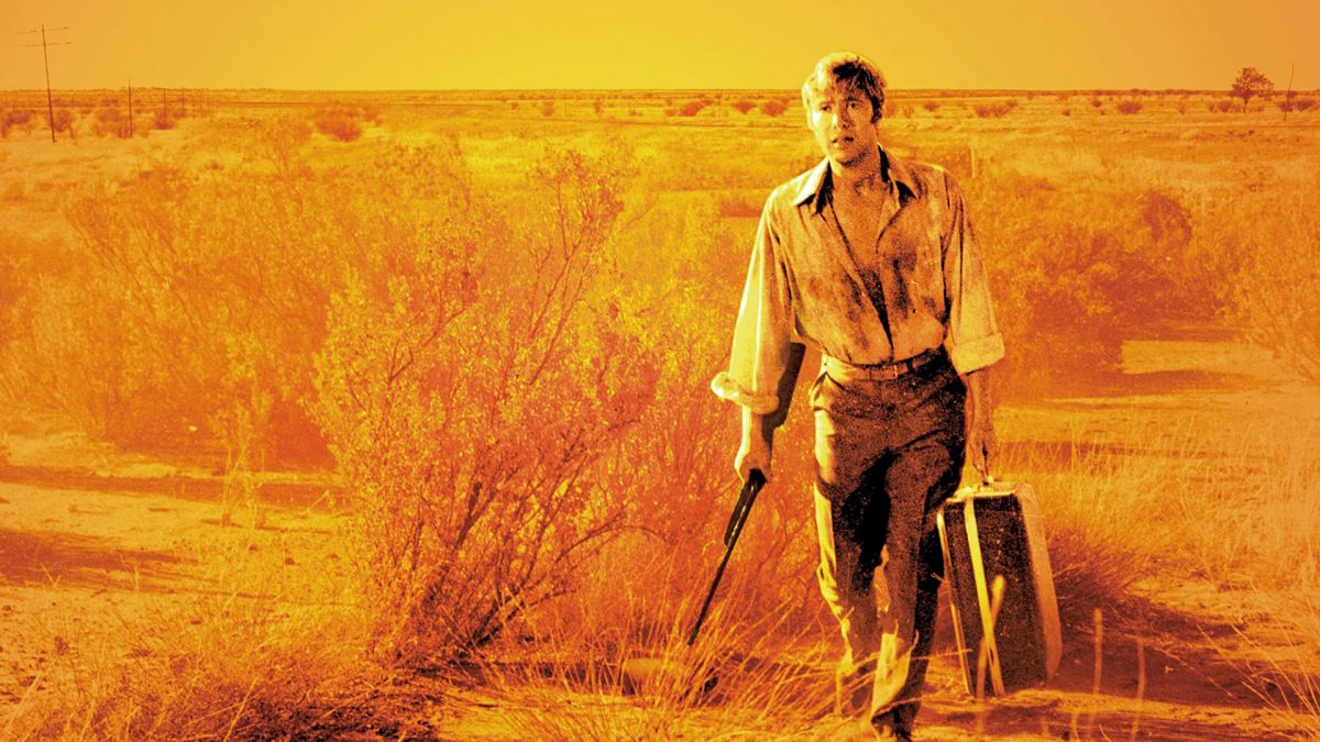 Promotional image for Wake in Fright showing a man in the desert with a rifle and a suitcase