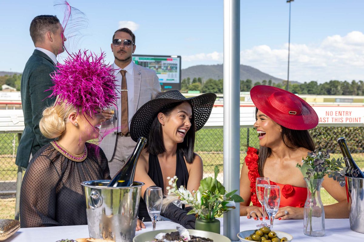 Three women smiling trackside at the races