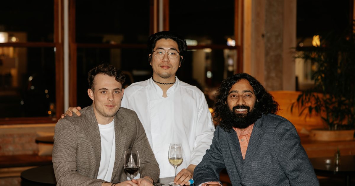 Three men pose in restaurant dining room.