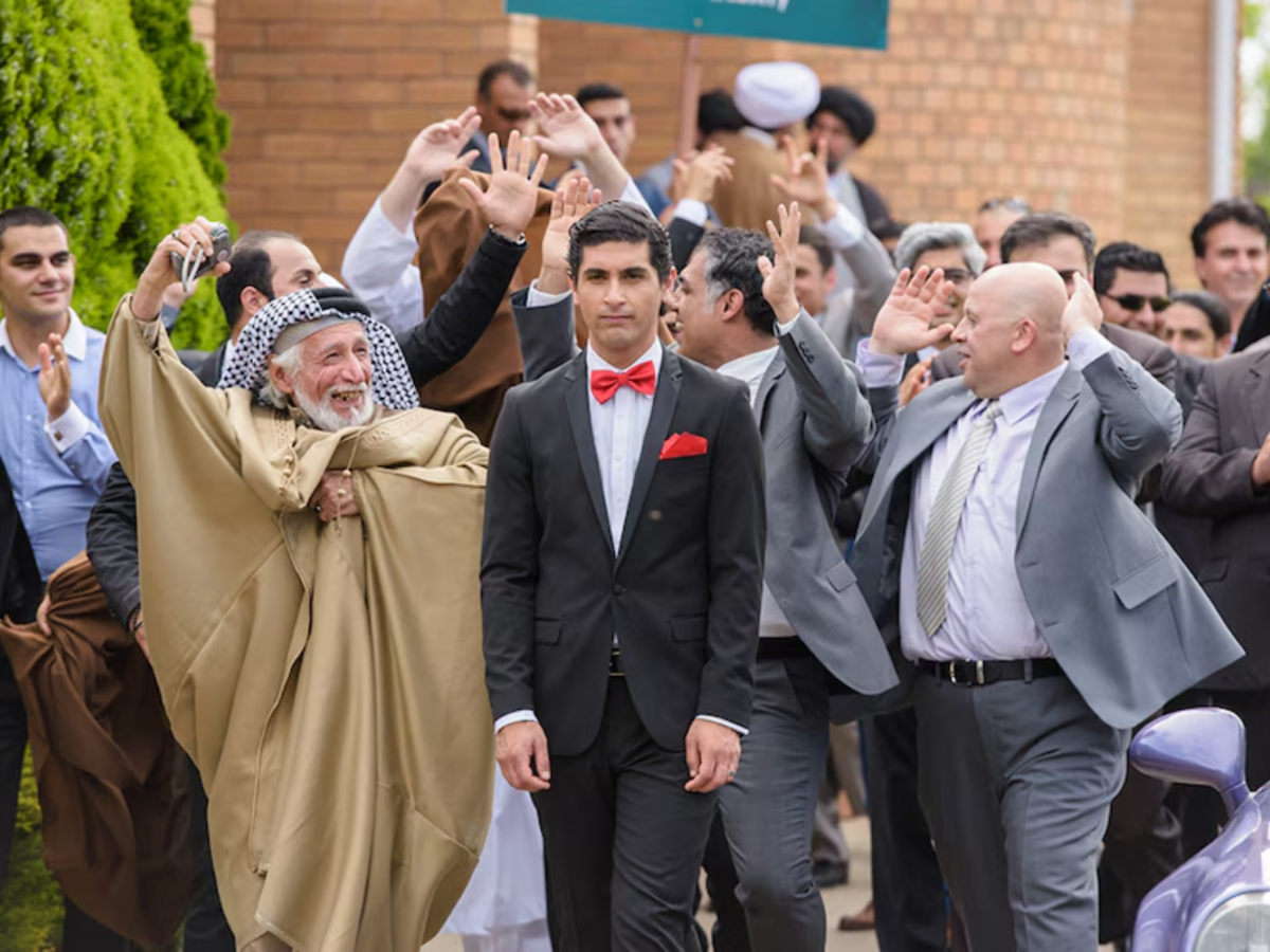 Still from Ali's Wedding showing a serious man surrounded by a cheering crowd