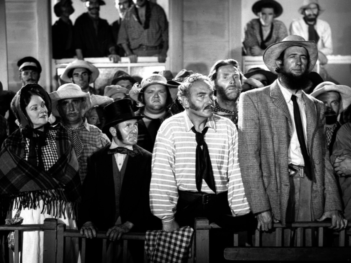 Black and white still from Eureka Stockade showing a room full of people dressed in 1800s attire