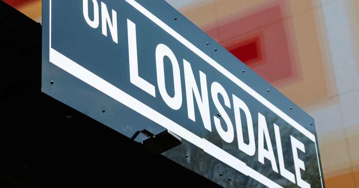 A black and white sign reading On Lonsdale with a red, orange and white mural in the background.