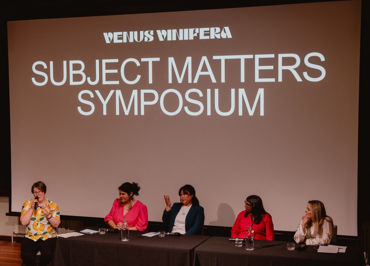 A panel of five women sit on a stage