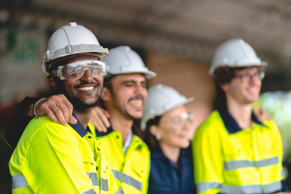 Four building workers in hardhats arm in arm on site
