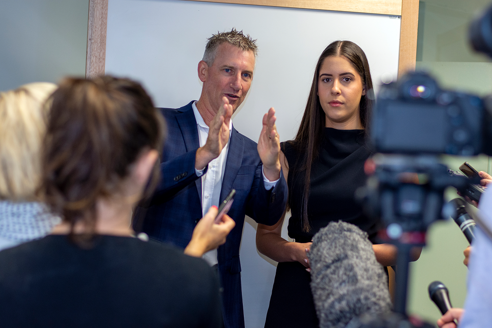 Cam Sullings talking to a person looking at a camera with people holding microphones