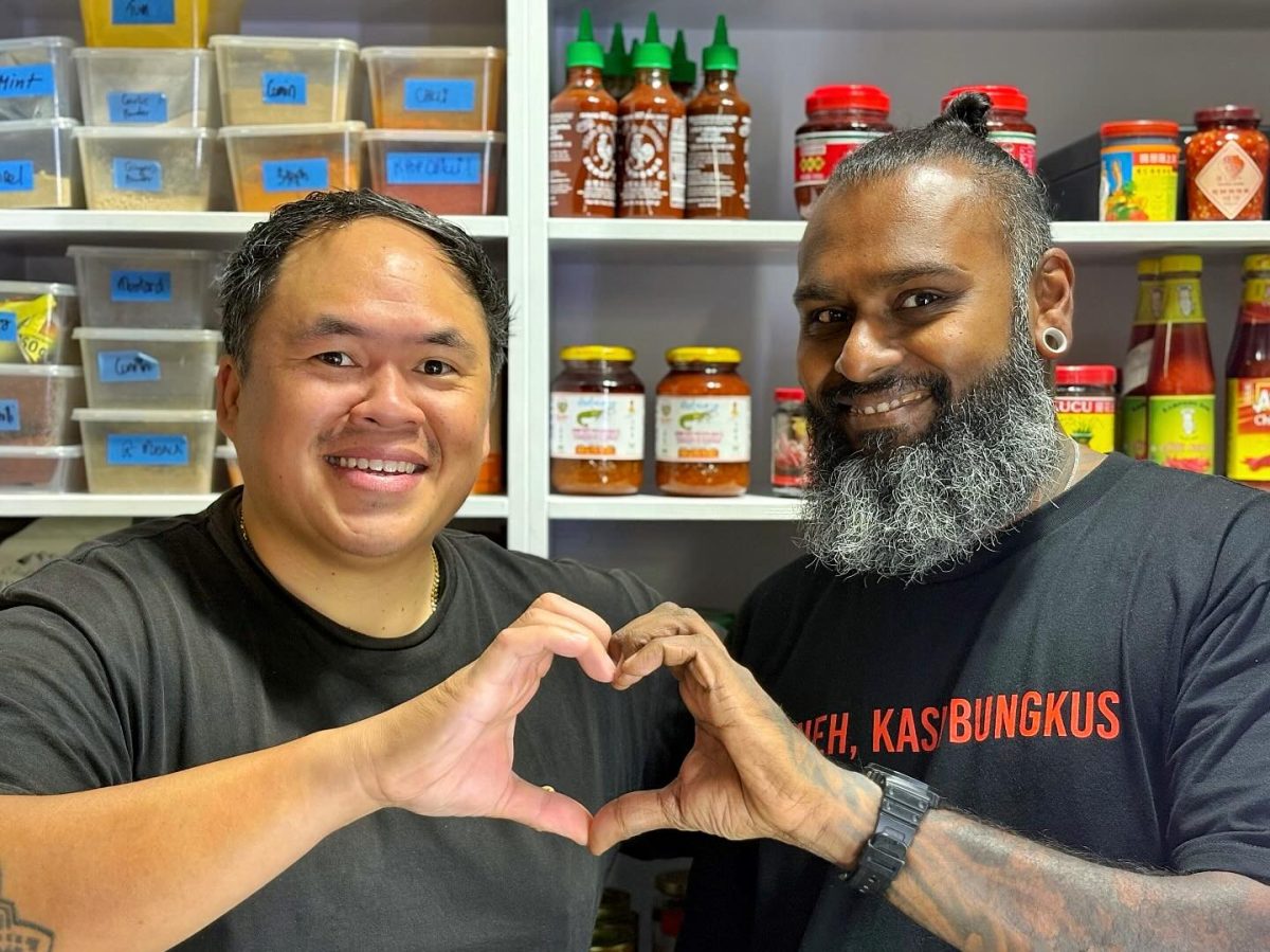 Andrew Duong and AK Ramakrishna stand side by side and create a heart shape with their hands.