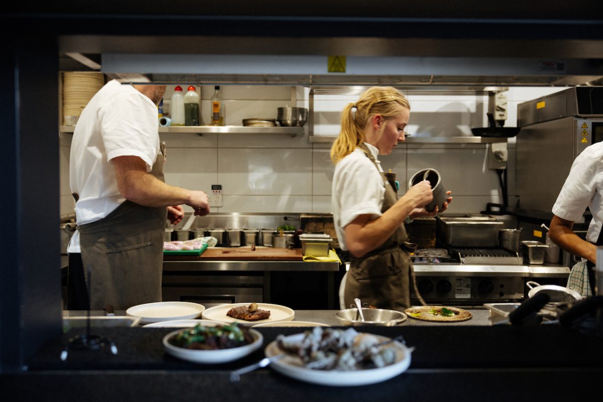 A female chef with blonde ponytail in the centre of a busy kitchen