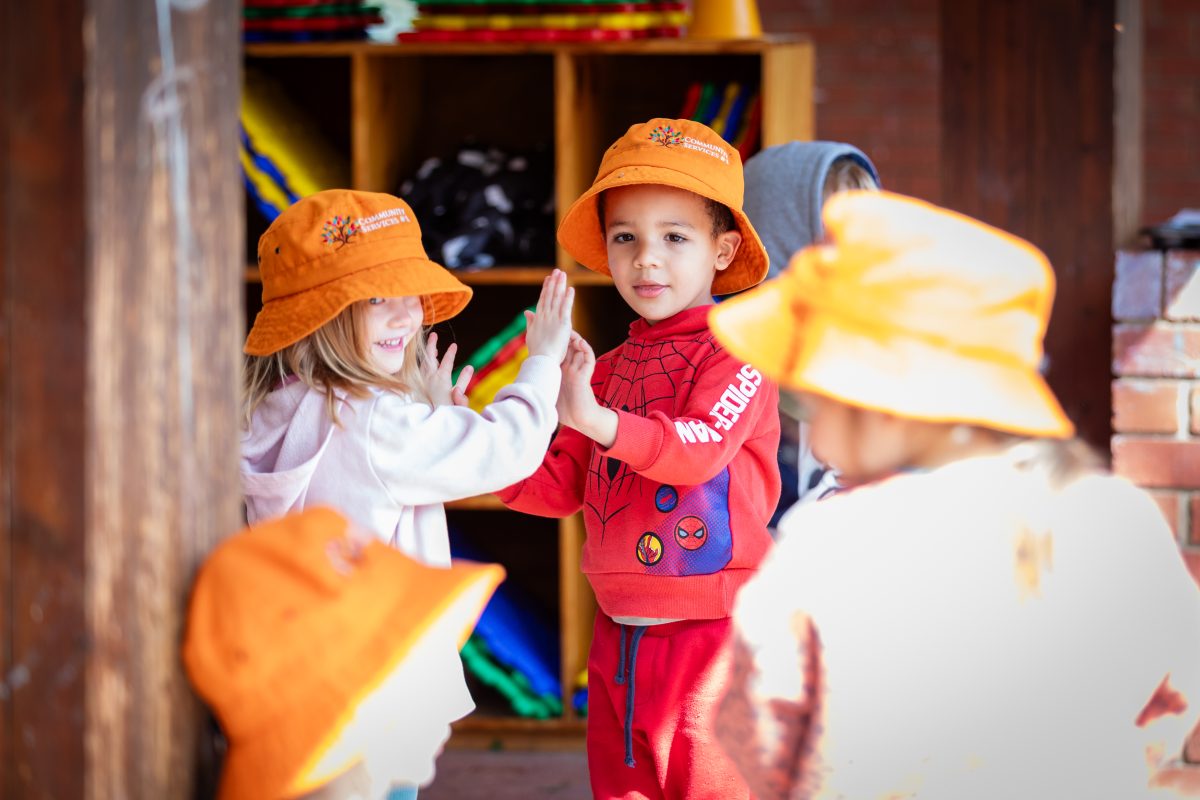 Two kids high fiving each other, one looking at the camera with a smile