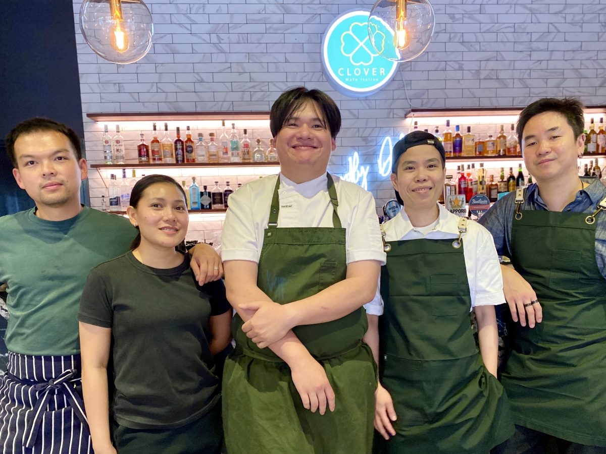 A group of five people in green aprons or shirts standing in front of a bar.