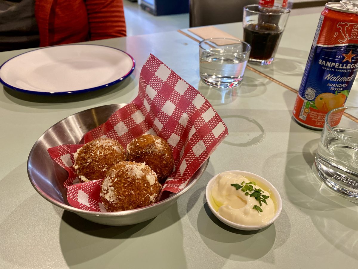 Three arancini balls in a bowl with a red and white checked piece of paper.