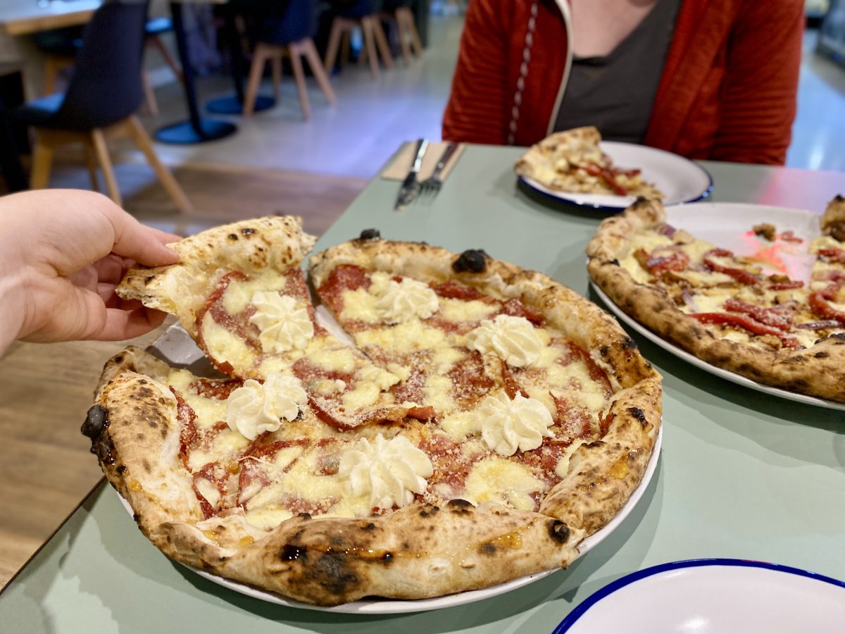 A hand lifts a slice of pizza adorned with a piped rosette of whipped ricotta.
