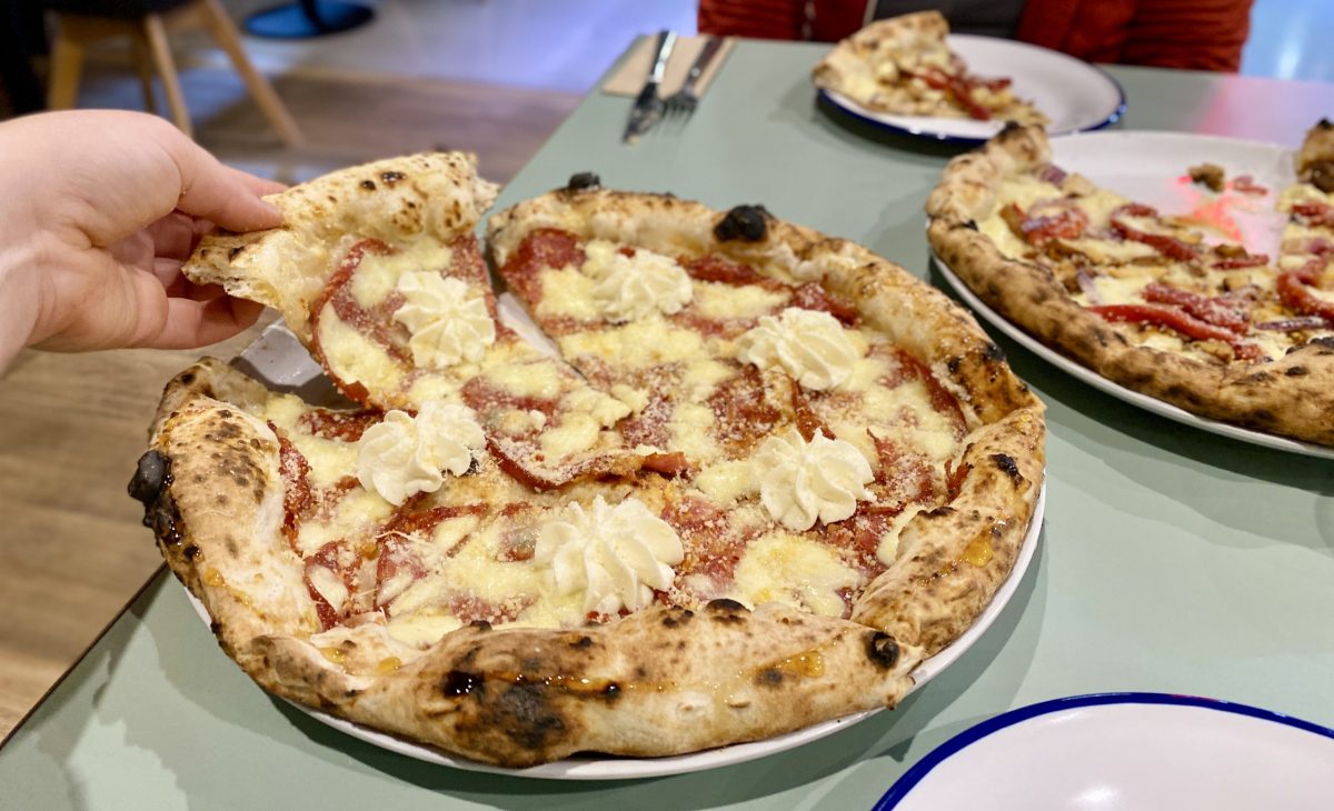 A hand lifts a slice of pizza adorned with a piped rosette of whipped ricotta.