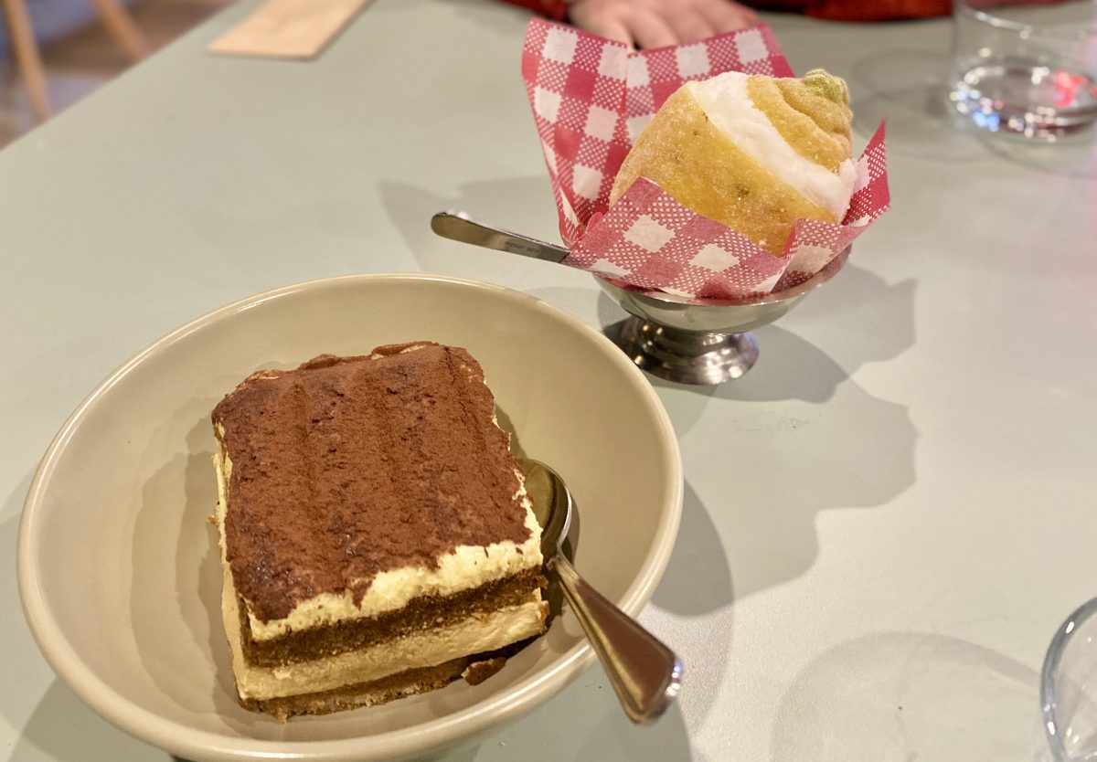 A generous portion of tiramisu in a bowl, behind it there is another bowl with a whole lemon filled with sorbet
