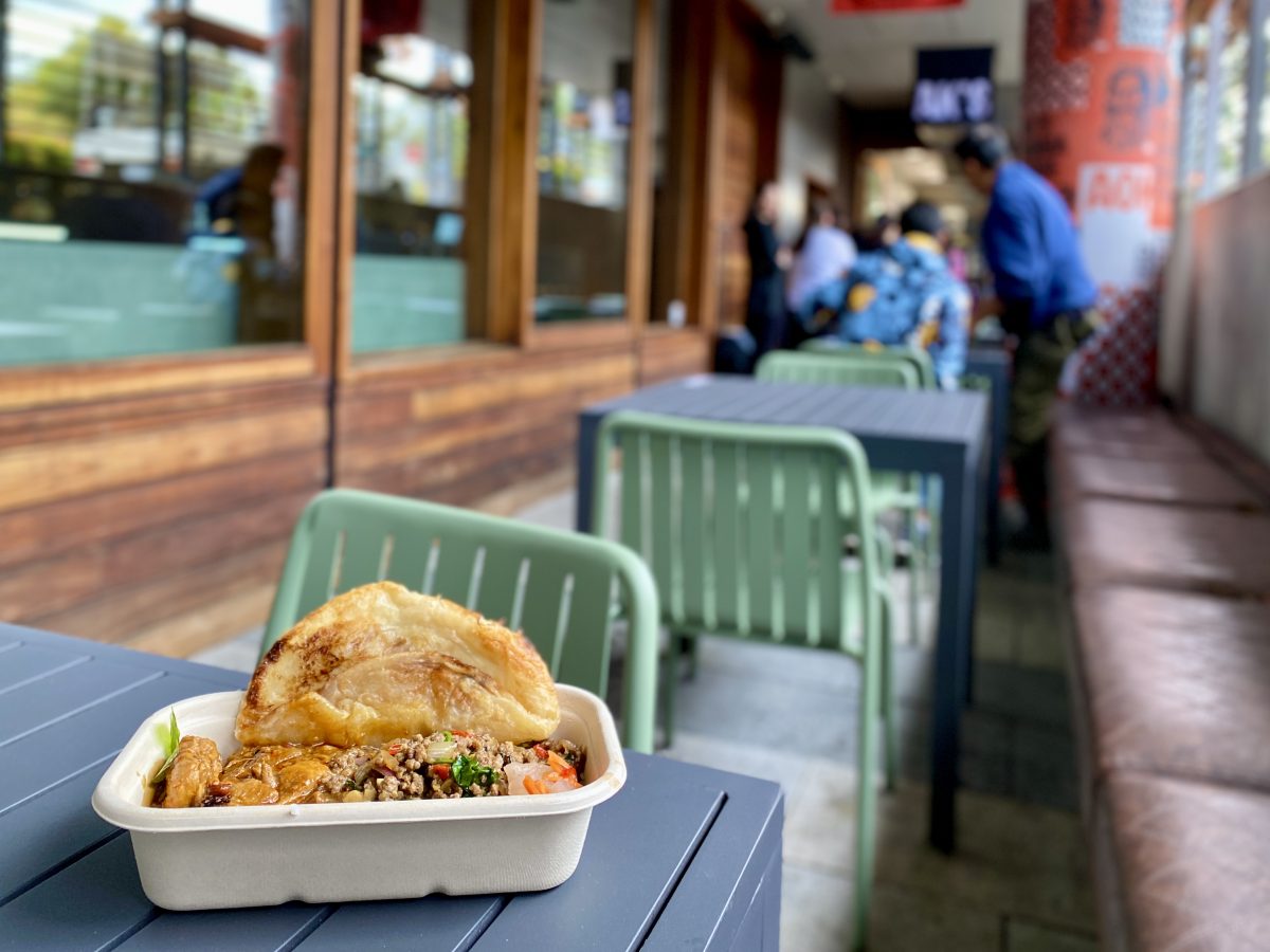 A takeout container of curries with a piece of roti.