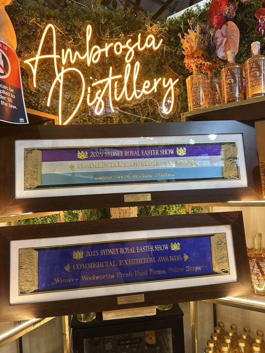 Two ribbon awards in frames under a neon sign reading Ambrosia Distillery.