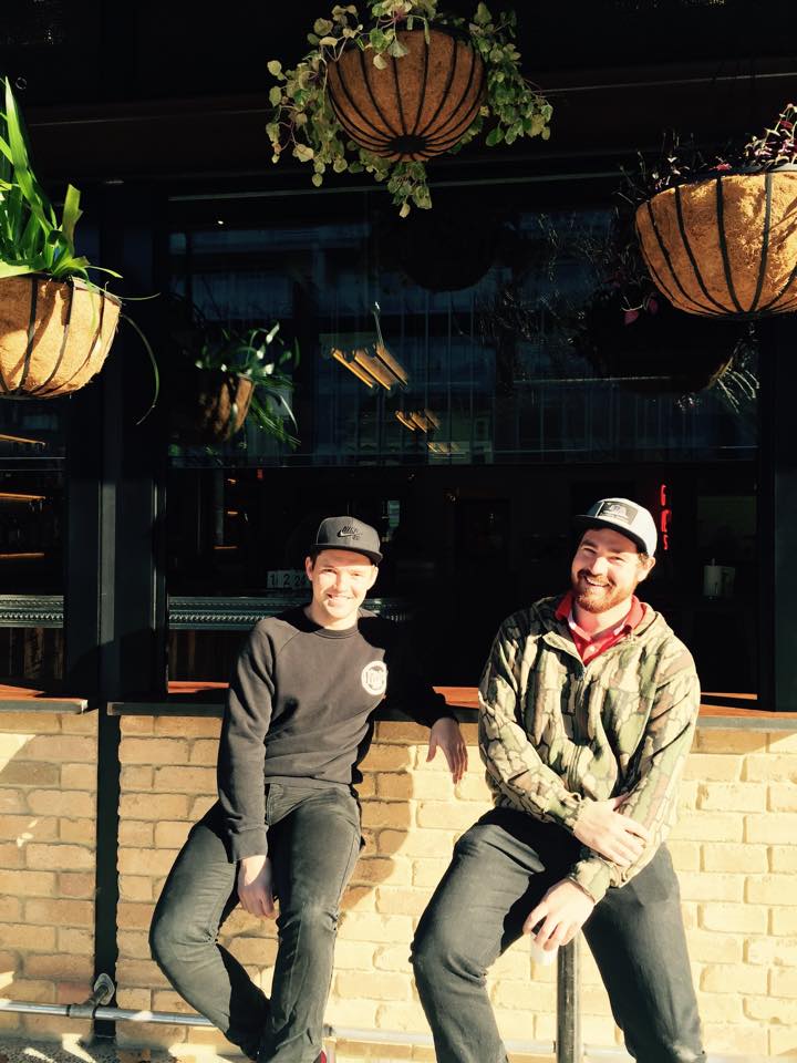 Two young men wearing caps sitting outside Grease Monkey when it first opened.