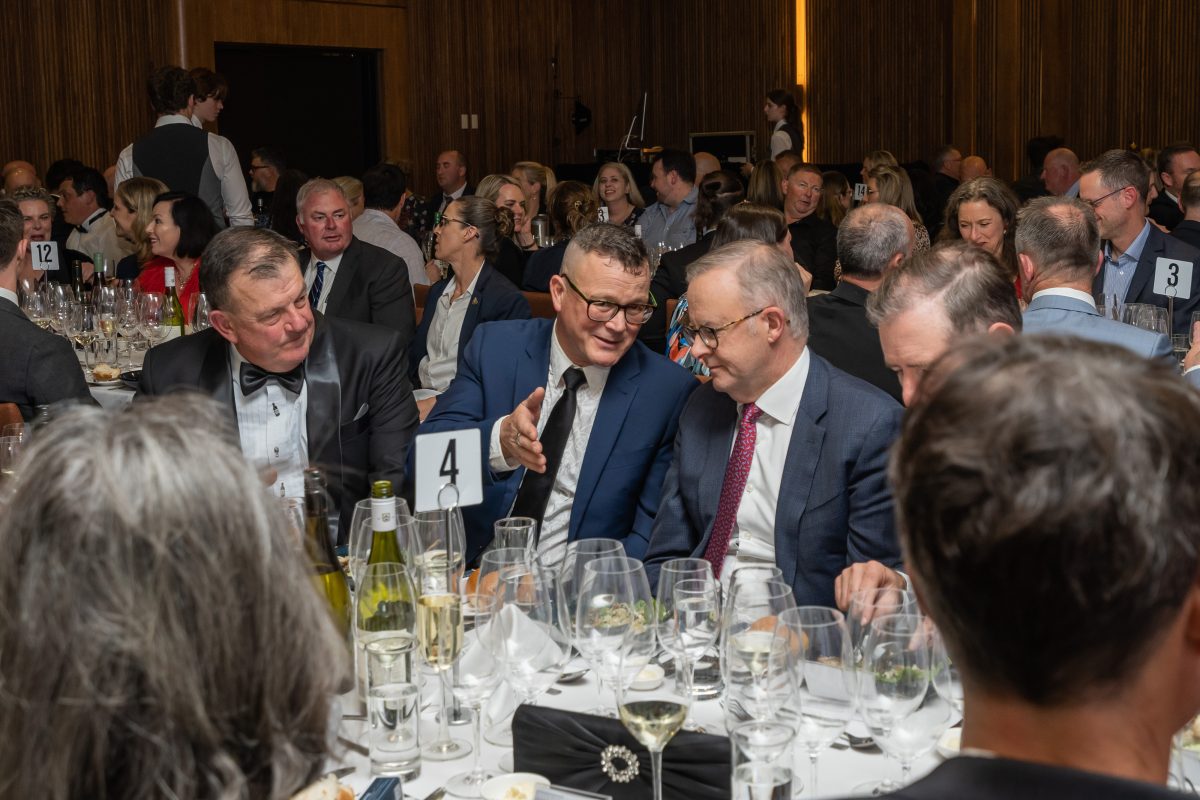 Prime Minister Albanese in conversation with a man in a suit at a table crowded with wine glasses.