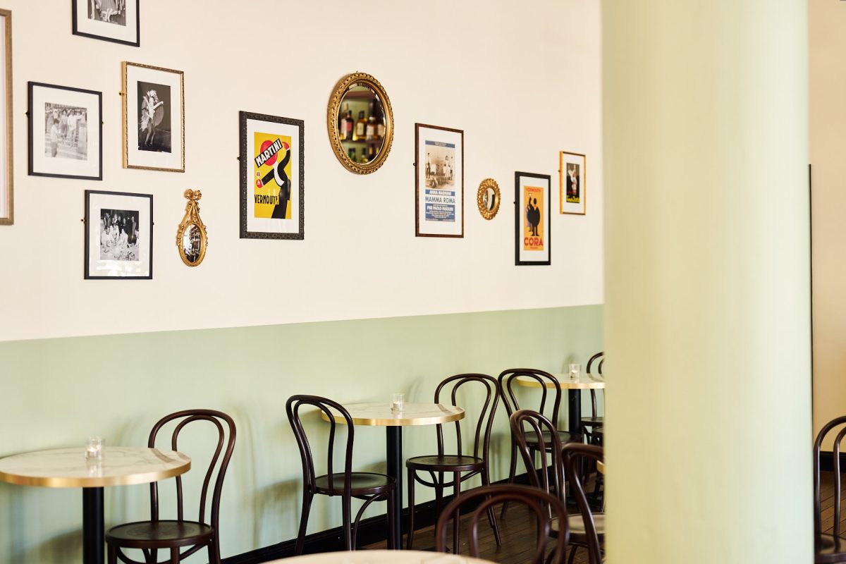A dining decorated with a two-tone mint green and cream wall, with vintage posters, bent wood chairs and marble tables. 