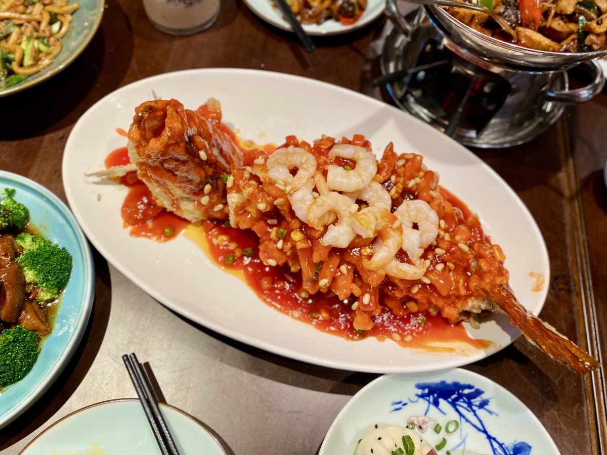 A whole fish cut intricately and doused in a red sauce. Prawns are scattered on top.