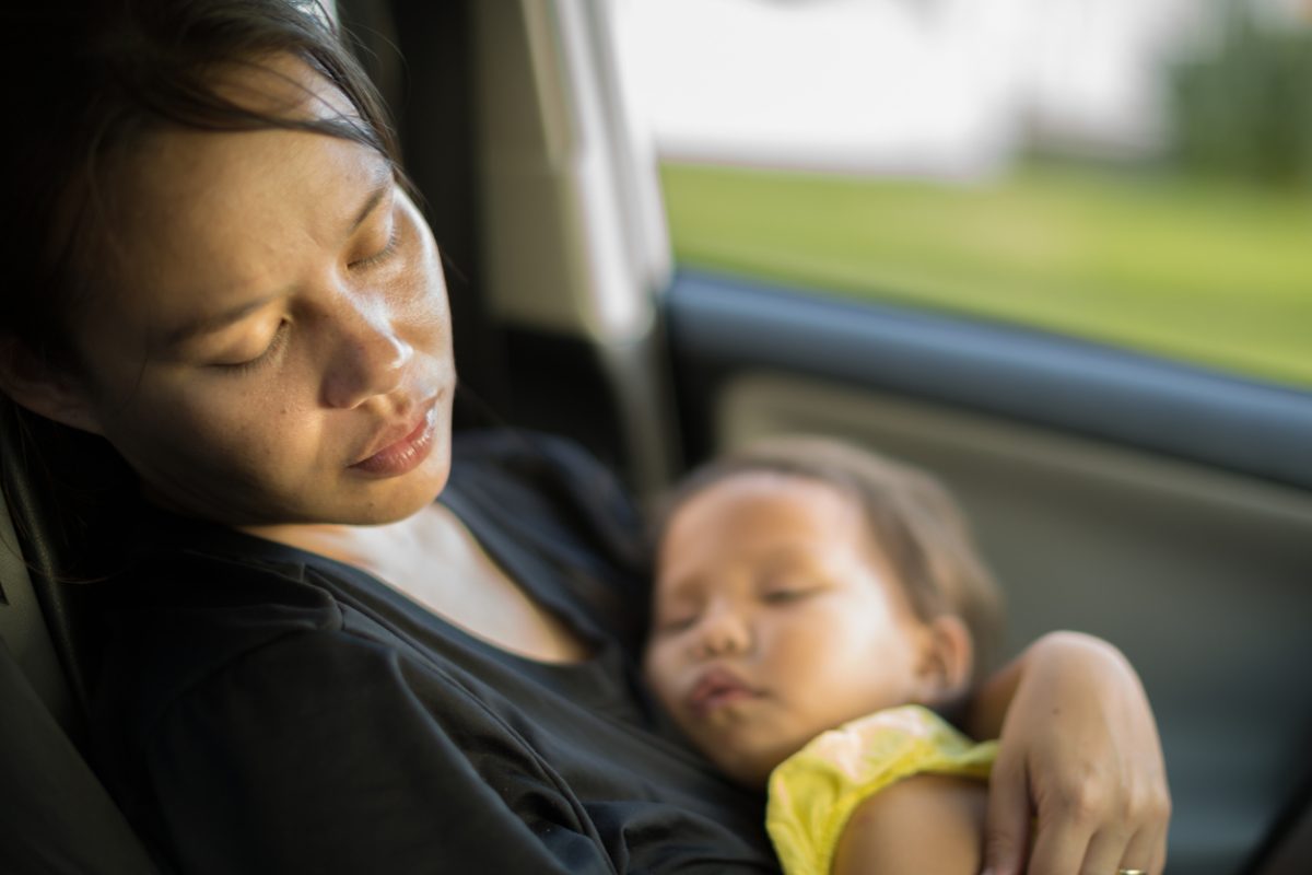 A mother sleeps in a car with her baby in arms