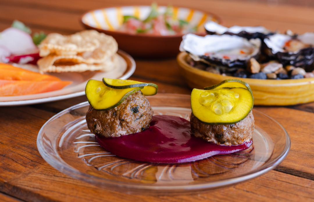 Two round pieces of cooked lamb topped with colourful zucchini and turmeric pickles on a beetroot puree.