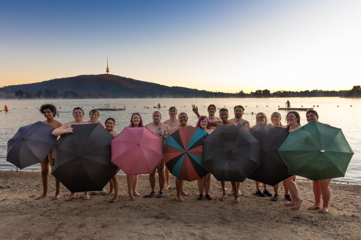 group of people nude behind umbrellas in front of lake
