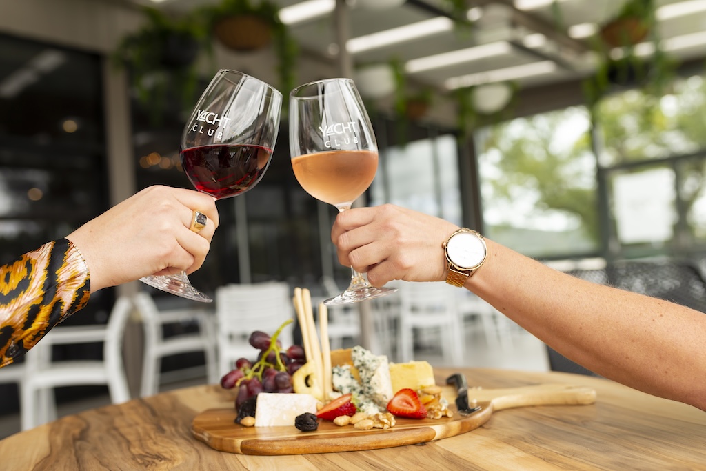 Two people cheersing wine glasses with a platter on the table.