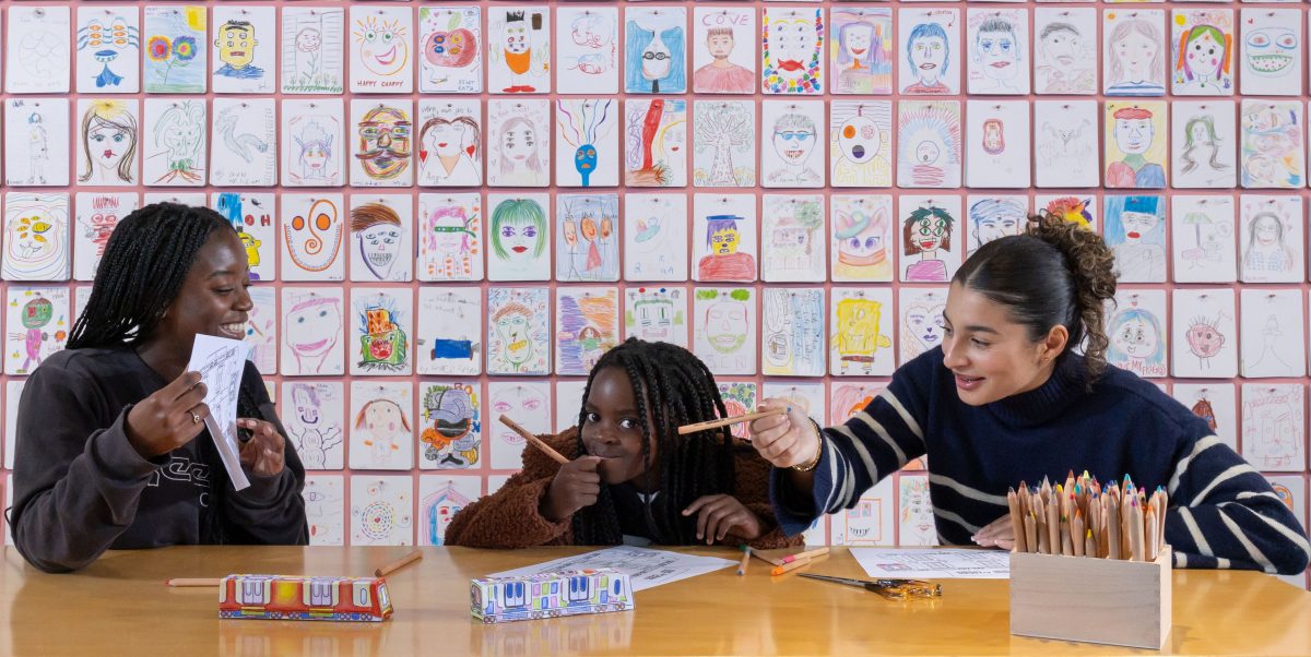 People sit in front of a wall of children's portraits and draw