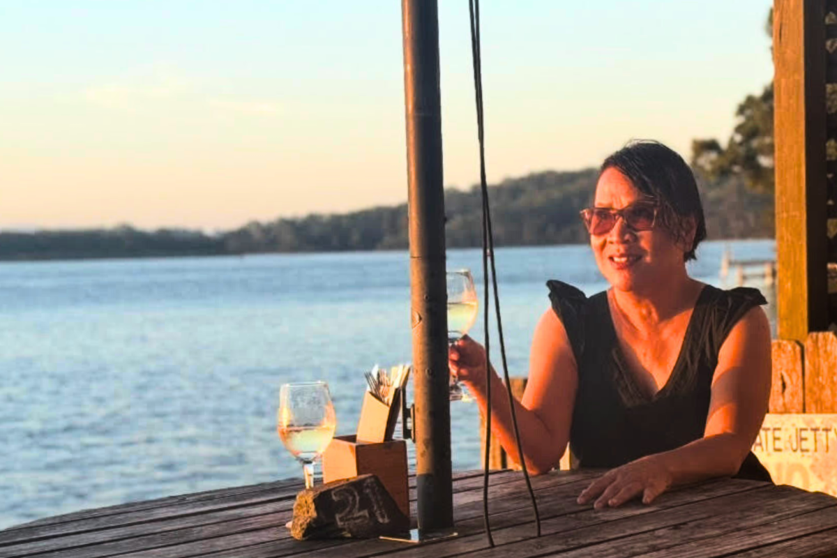 Bee Creevy holding drink in front of water.