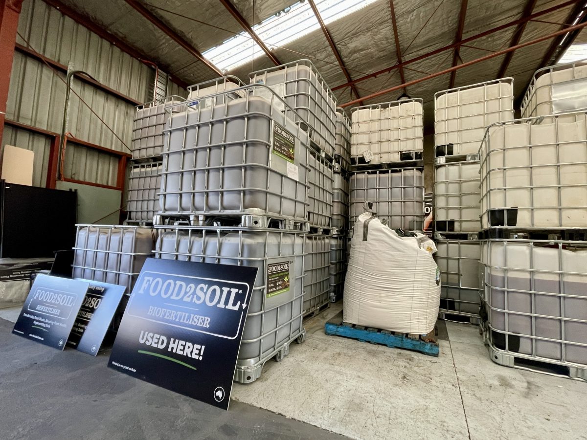Industrial IBC containers of Food2Soil biofertiliser with a sign reading "Food2Soil Used Here!"