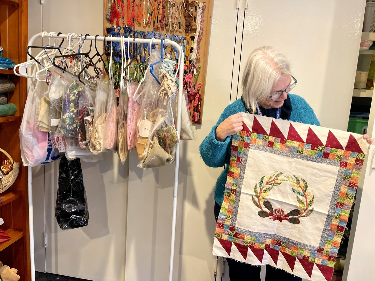 A woman holds up an unfinished piece of patchwork.