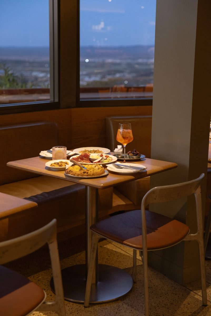 A warmly lit restaurant table at dusk with flatbread, cocktails and other dishes.