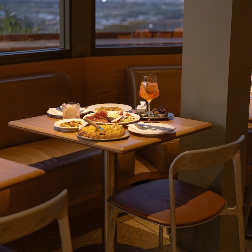 A warmly lit restaurant table at dusk with flatbread, cocktails and other dishes.