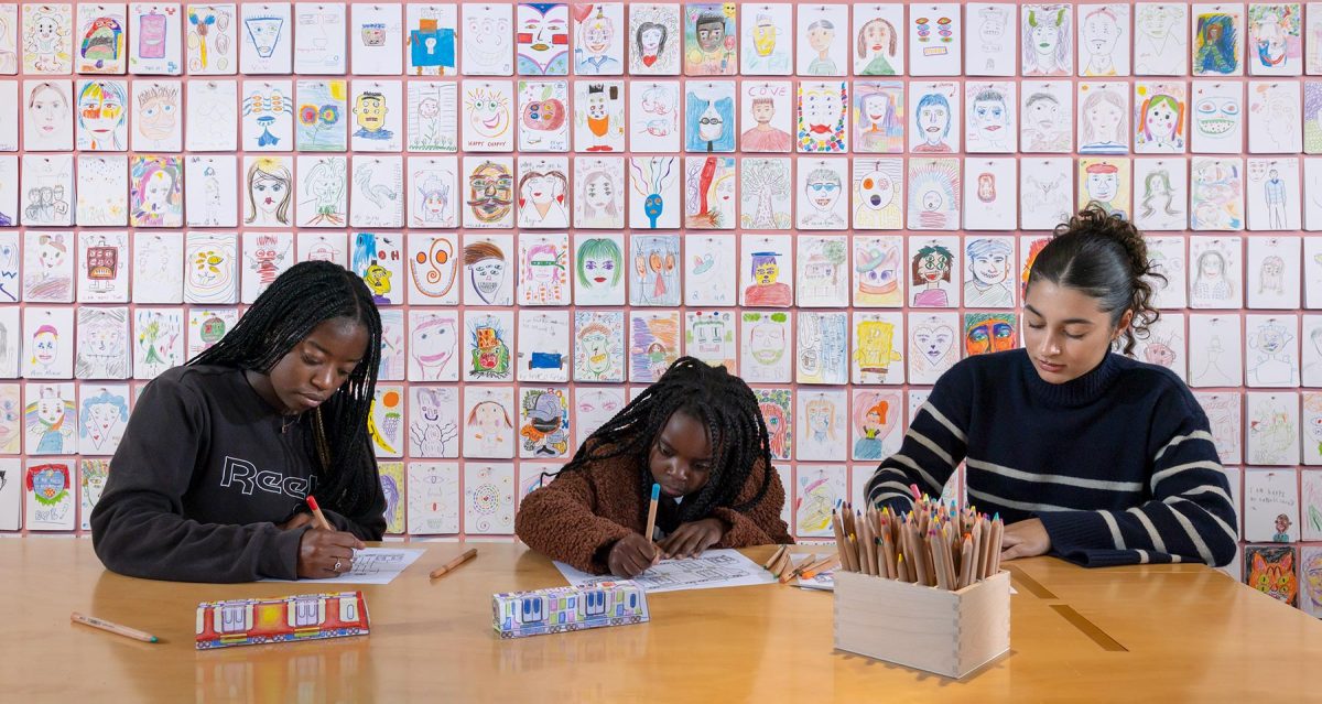 3 children sitting at a desk drawing with pencils and paper