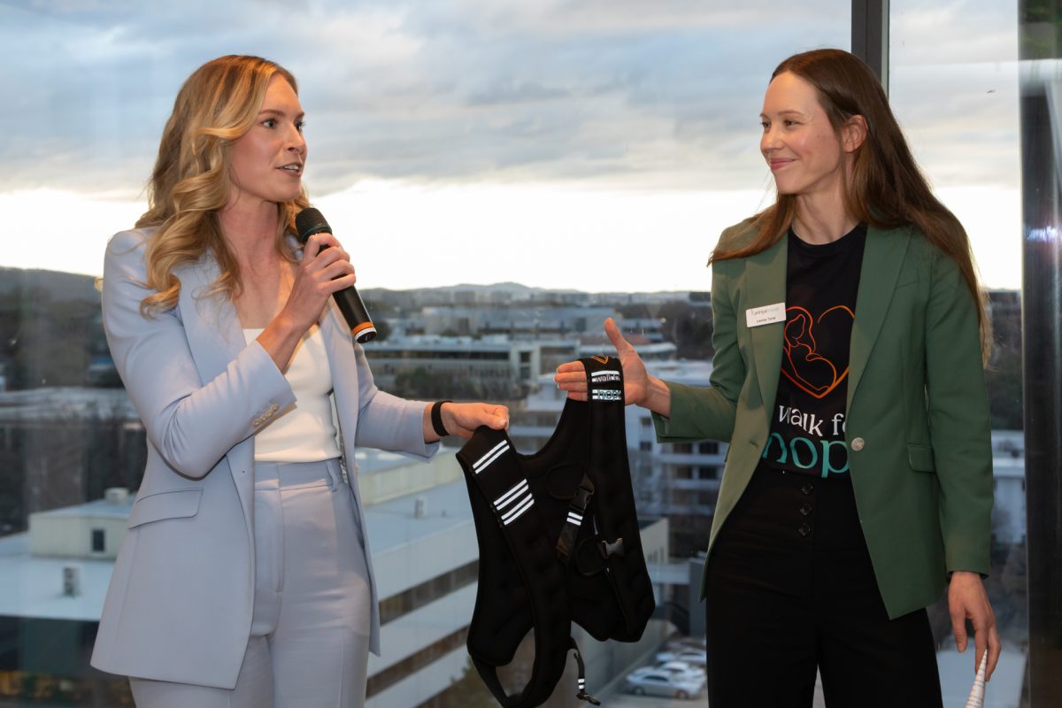 Holly Ferling and Lavinia Tyrrel hold a weighted vest as Holly speaks into a microphone