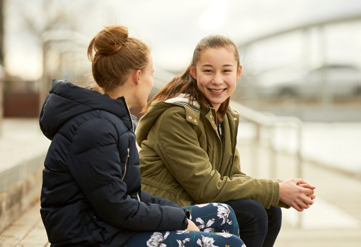 girl smiling at camera, sitting next to friend
